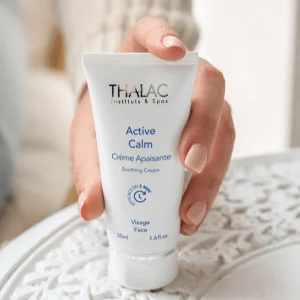 Main de femme tenant un flacon de crème Active Calm posé sur une table blanche