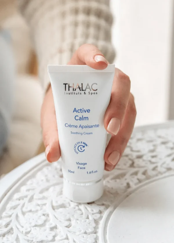 Main de femme tenant un flacon de crème Active Calm posé sur une table blanche