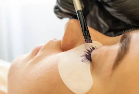 main gantée noir avec un pinceau teintant des cils