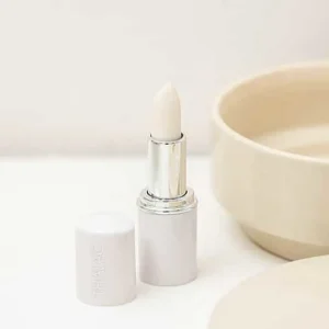 Stick à lèvre débouché avec le bouchon à côté posé au bord dans une salle de bain