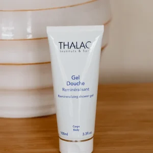 Flacon de gel douche reminéralisant devant un pot blanc sur une table en bois