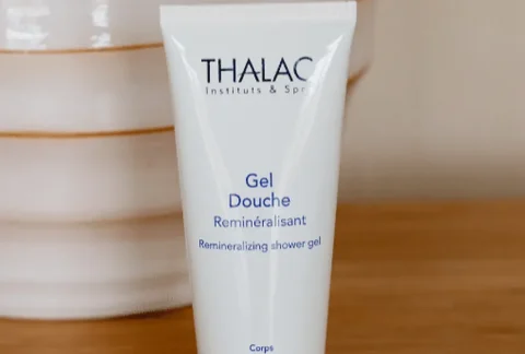 Flacon de gel douche reminéralisant devant un pot blanc sur une table en bois