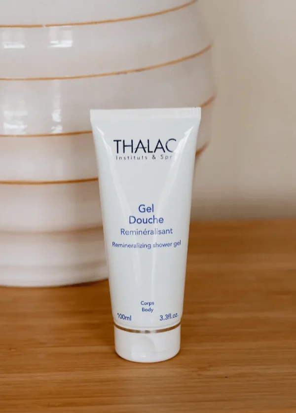 Flacon de gel douche reminéralisant devant un pot blanc sur une table en bois