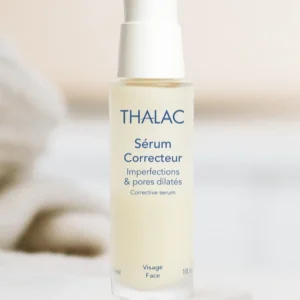 Flacon blanc et jaune de sérum correcteur posé au bord d'une table blanche