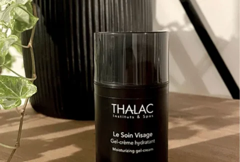 Flacon de soin visage noir posé sur une table en bois devant une plante