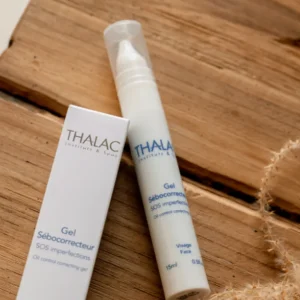 Flacon de gel sébocorrecteur allongé sur un table à côté de sa boite en carton blanche