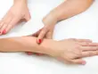 Deux mains avec du vernis rouge retirant une bande d'épilation sur un avant-bras