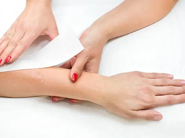 Deux mains avec du vernis rouge retirant une bande d'épilation sur un avant-bras
