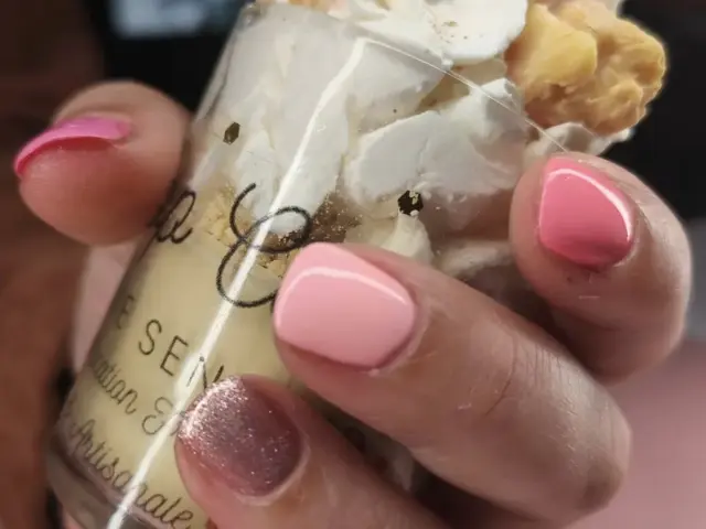 Main tenant un pot de glace avec du vernis sur les ongles de différentes couleurs
